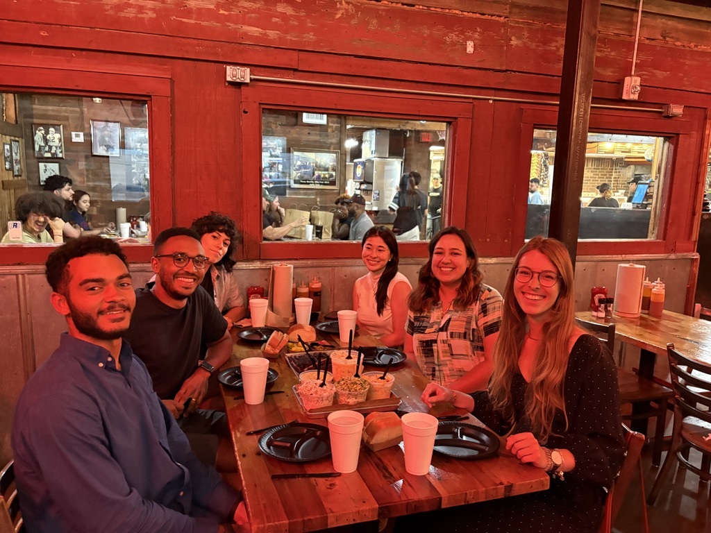 Co-Design Lab members Douglas, Kosa, Yakira, Elisa, Nicole, and Gaelle sitting at a table with barbeque sitting on the table in front of them